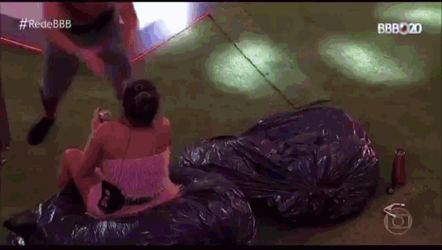 a man and a woman are sitting on a pile of trash bags on the floor .
