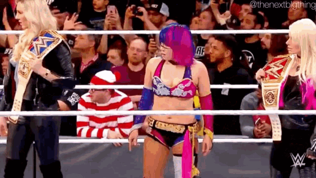 a woman with purple hair is standing in a wrestling ring with other women and a man in a santa hat .