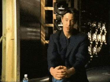 a man in a suit is sitting with his hands folded in front of a bottle of water
