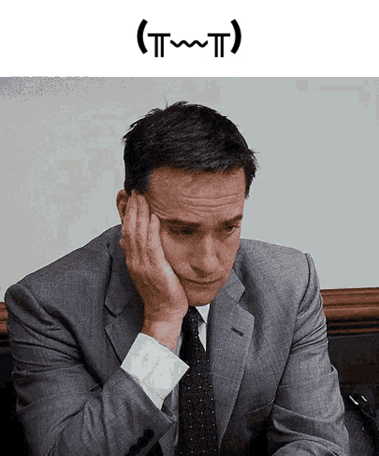 a man in a suit and tie is sitting at a desk with his hand on his forehead .