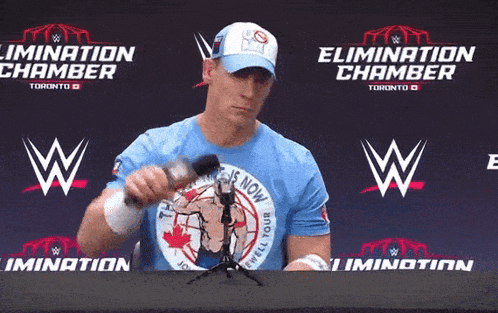a man wearing a blue shirt that says elimination chamber is holding a microphone