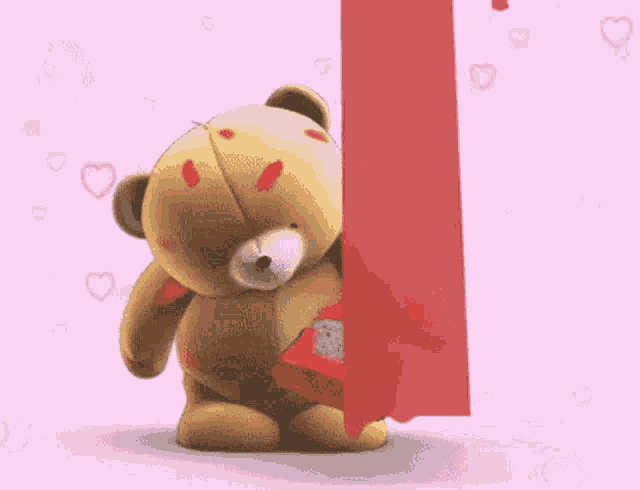 a teddy bear is standing next to a red item