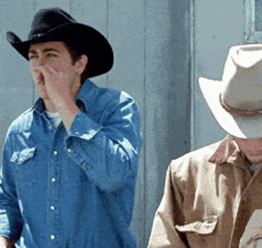 a man wearing a cowboy hat and a denim shirt covering his nose