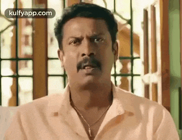a man with a mustache and a necklace is making a funny face .
