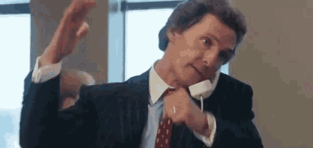 a man in a suit and tie is talking on a cell phone in front of a window .