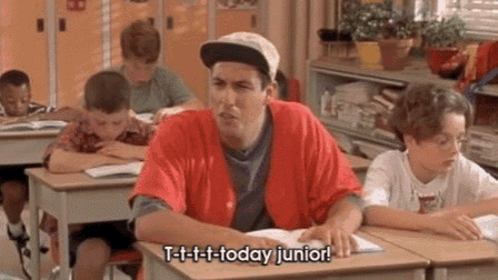 a man in a red shirt is sitting at a desk in a classroom talking to a boy .
