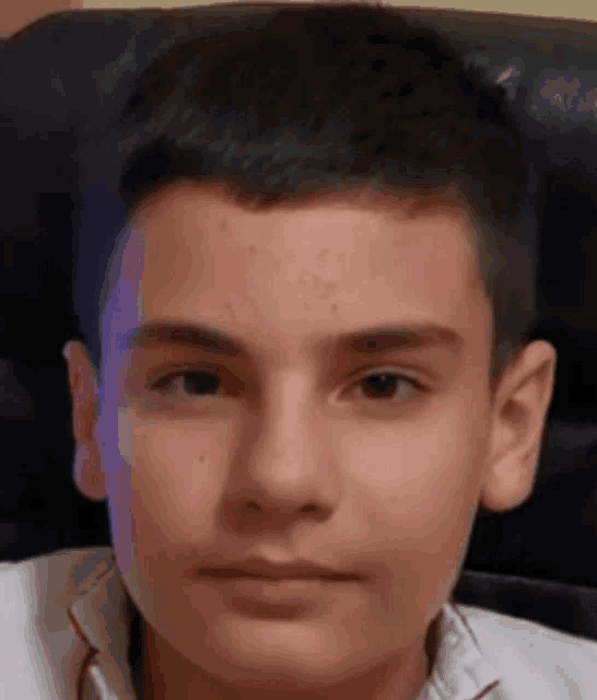 a young boy with short hair is sitting in a chair looking at the camera .