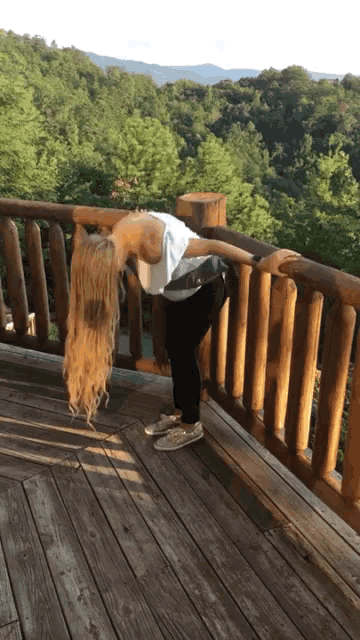 a woman stands on a wooden deck overlooking the mountains