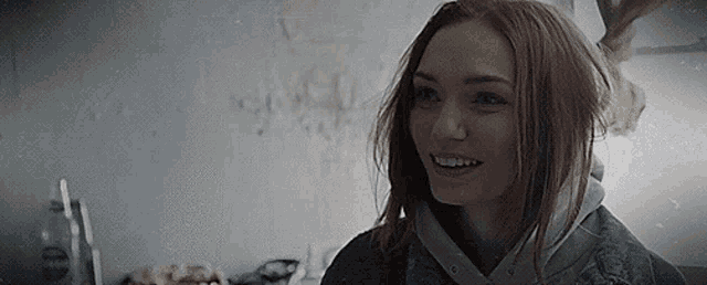 a woman with red hair is smiling in front of a white wall .
