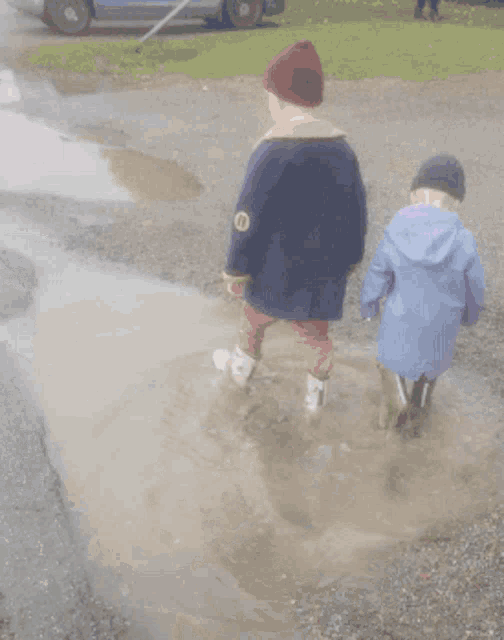 two children are walking through a puddle with a patch on their jacket that says ' i '