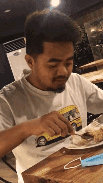 a man in a white shirt with a yellow school bus on it is eating food