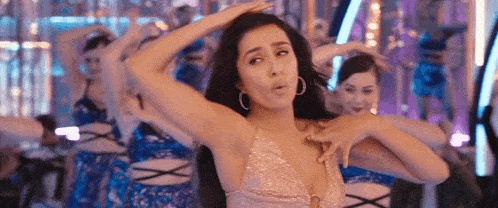 a woman in a pink dress is dancing with a group of dancers in a room .