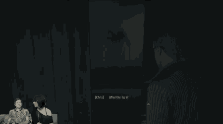 a group of people are sitting on a couch in a dark room while a man is standing in the doorway .