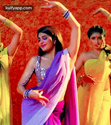 a woman in a purple sari is dancing with two other women in yellow dresses .