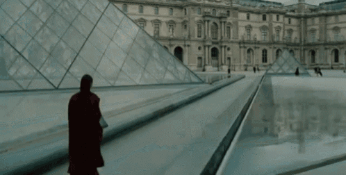 a man in a red coat is walking in front of a building with pyramids