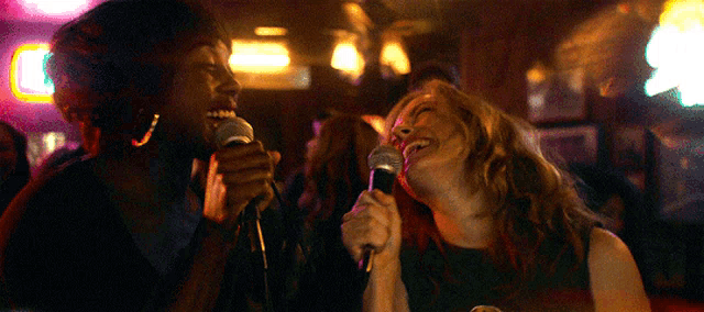 two women are singing into microphones in a bar