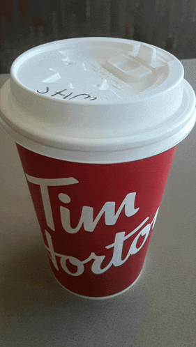 a red tim hortons cup with a white lid sitting on a table