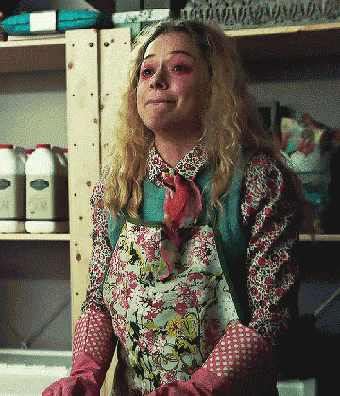 a woman wearing a floral apron and pink gloves stands in front of a shelf with bottles of milk on it
