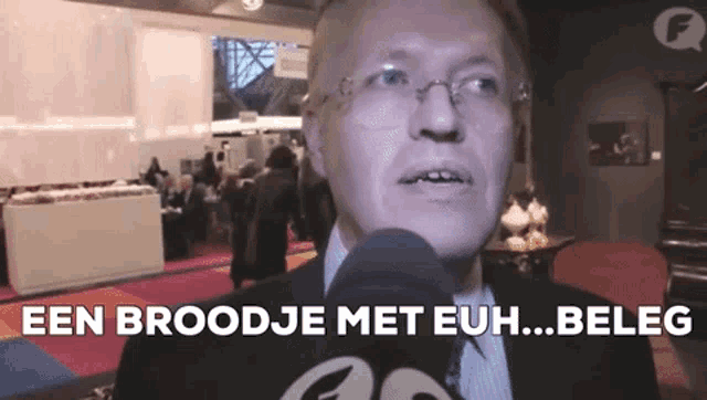 a man in a suit and tie is talking into a microphone and says een broodje met euh ... beleg ..