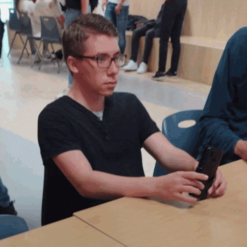 a man wearing glasses sits at a table with a cell phone in his hand