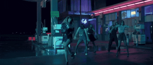 a group of girls are dancing in front of a gas station at night .