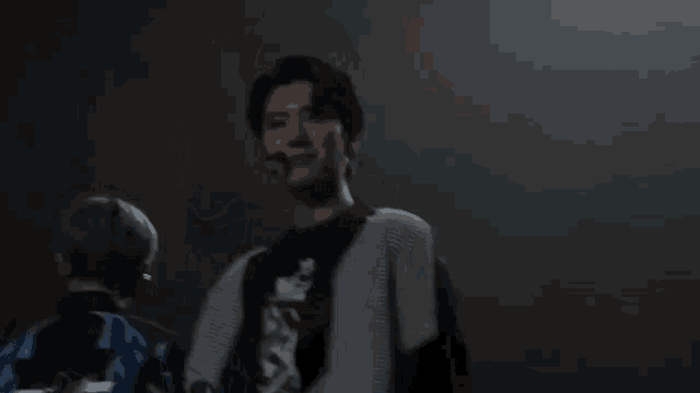 a man in a gray and black sweater is waving his hand in a dark room .