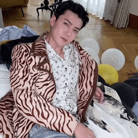 a man wearing a zebra print jacket is laying on a bed with balloons .