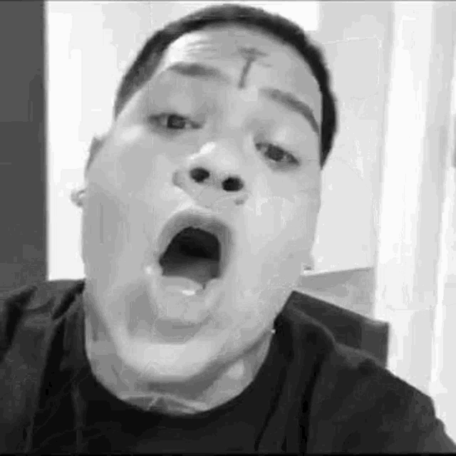 a man with a cross tattoo on his forehead is making a funny face .