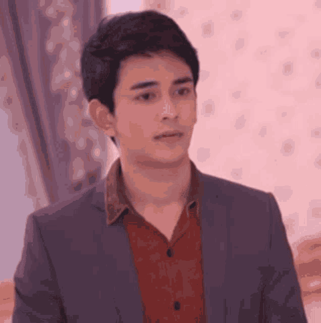 a man in a suit and red shirt is standing in front of a pink wall .