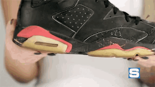 a person is holding a black and red shoe with the letter s in the corner
