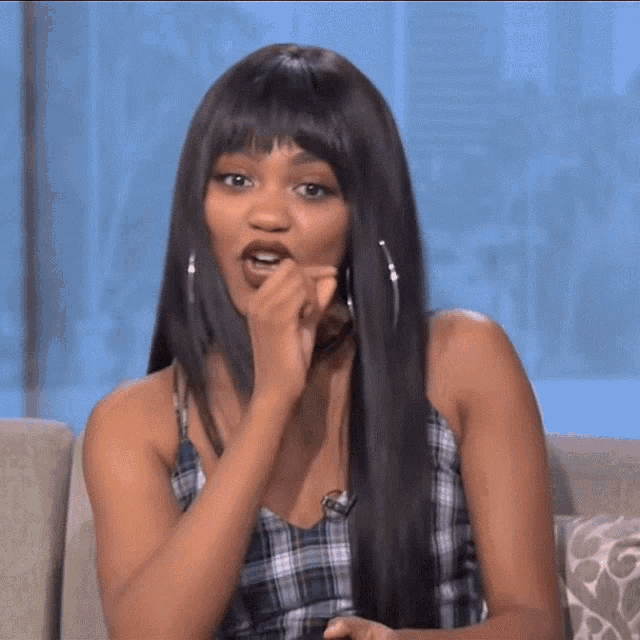 a woman with long black hair is sitting on a couch making a face