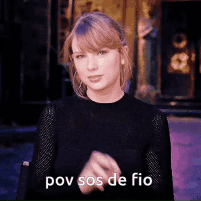 taylor swift is wearing a black sweater and making a gesture with her hands .