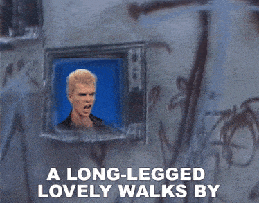 a long legged lovely walks by with a picture of a man on the screen