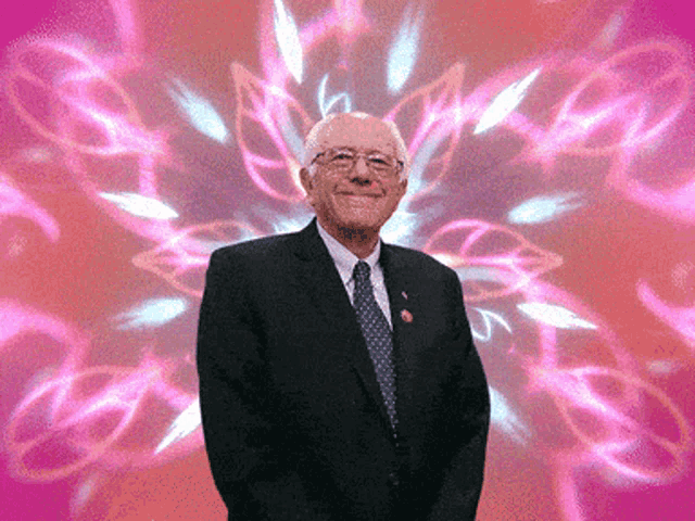 a man in a suit and tie smiles in front of a pink background