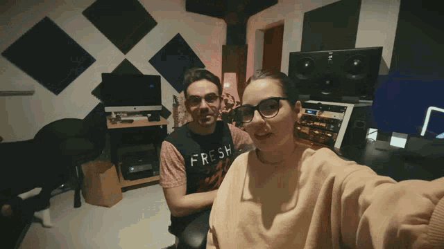 a man wearing a shirt that says fresh sits next to a woman in a room