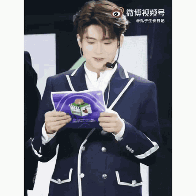 a man wearing a suit and a microphone is holding a piece of paper that says ' chinese ' on it