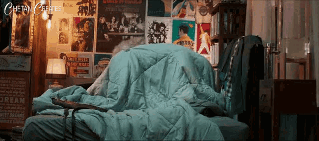 a bed with a blue blanket and posters on the wall including one for freddie mercury