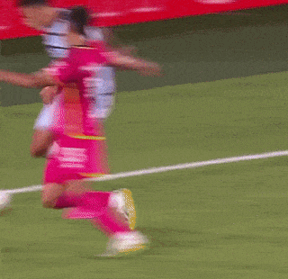 a blurred image of a soccer game with a red wall behind the players
