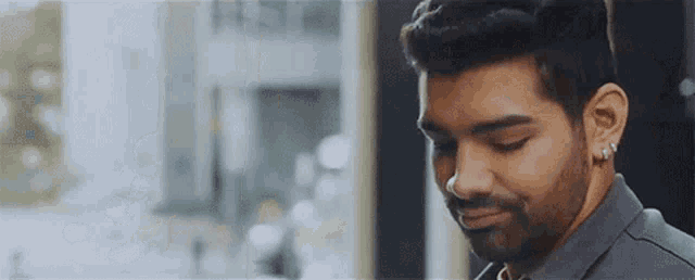 a man with a beard and earrings is smiling while looking down .