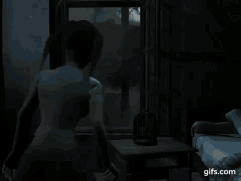 a person is standing in a dark room looking out a window .