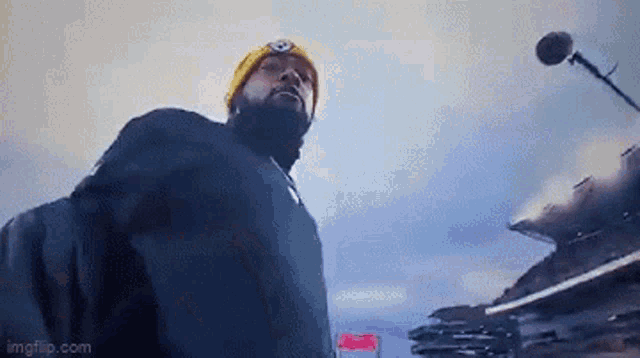 a man with a beard wearing a yellow hat is standing in front of a microphone .