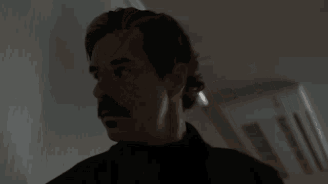 a man with a mustache is standing in a dark room in front of a wall .