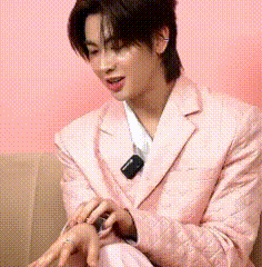 a young man in a pink suit is sitting on a couch with his hands on his lap .