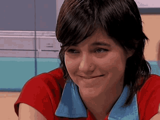 a woman with short hair is smiling and wearing a red shirt and blue collar .
