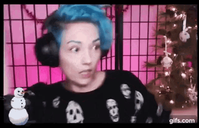 a woman with blue hair is wearing headphones and a skull sweater .