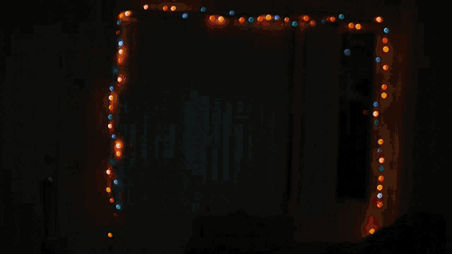 a man with blood on his shirt stands in front of a string of christmas lights