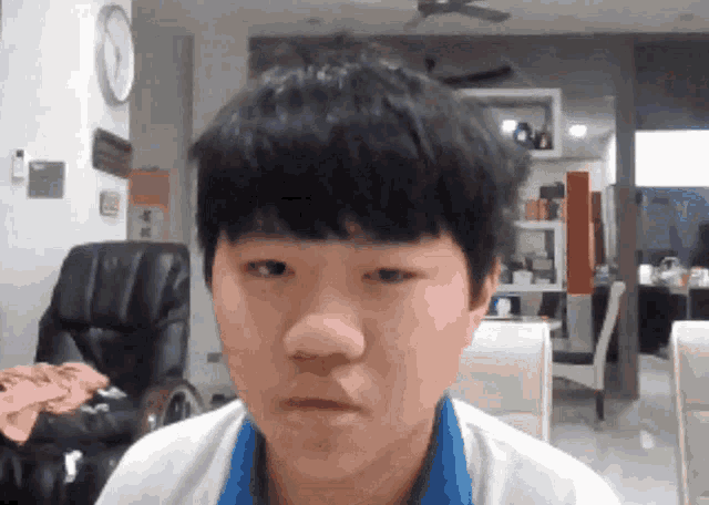 a young boy looks at the camera with a clock on the wall behind him