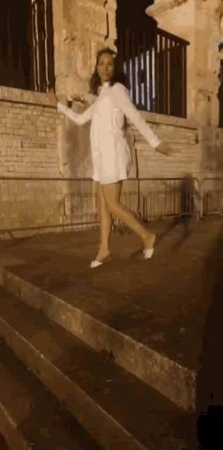 a woman in a white dress stands on a set of stairs