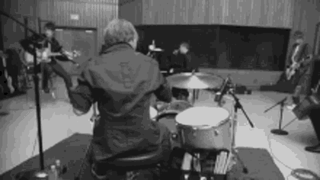 a man is sitting on a chair playing drums in a black and white photo .