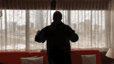 a man in a black jacket stands in front of a window with white curtains